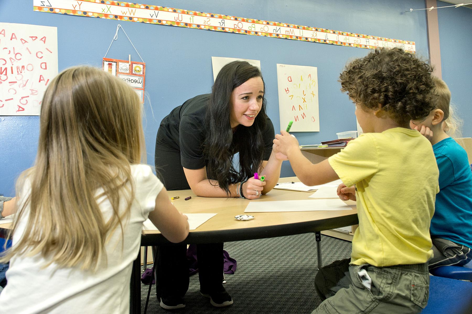 Mount Union student leans over table to assist three young children with learning activity